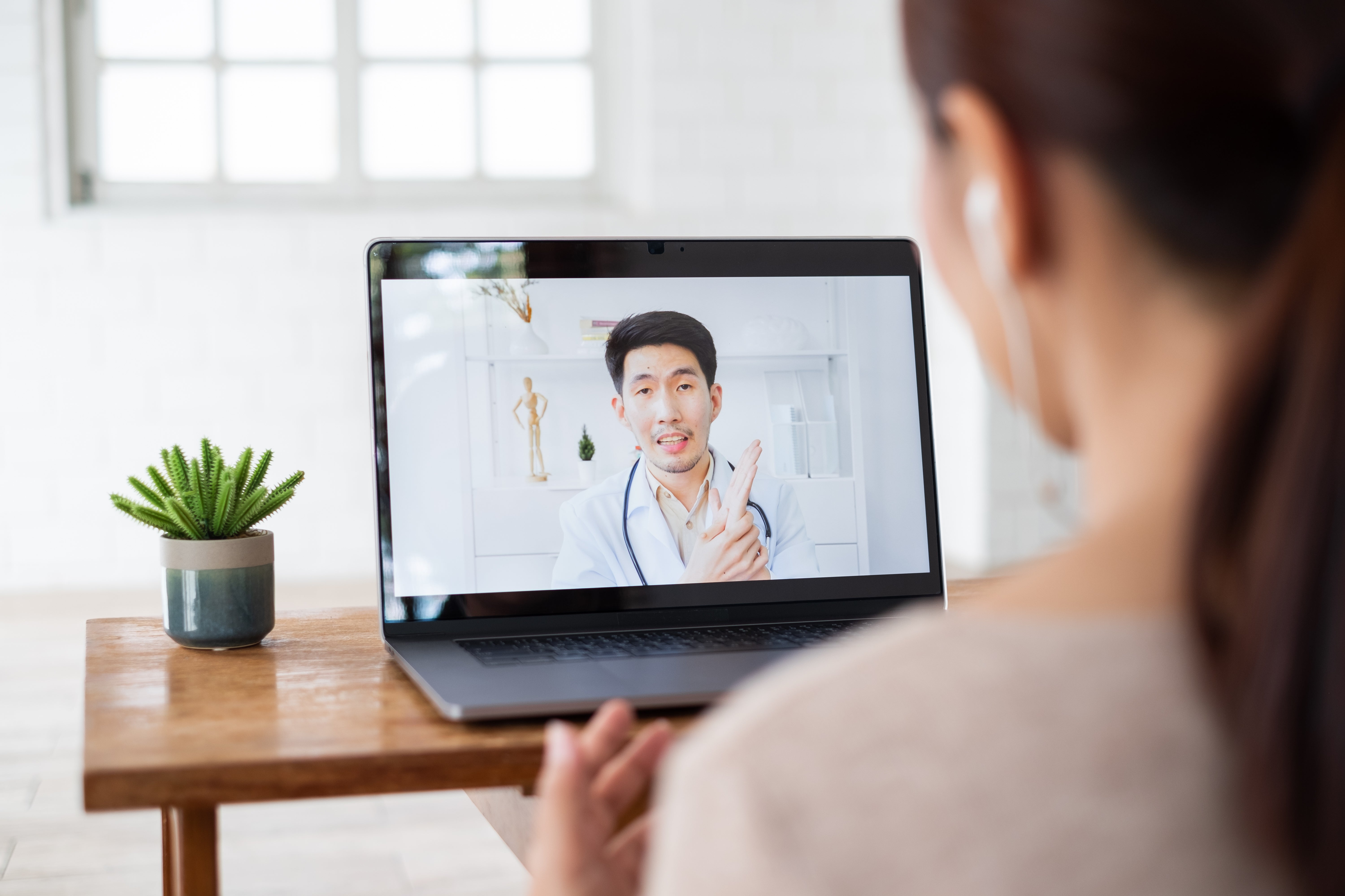 A telehealth appointment showing a doctor on a laptop speaking to a patient sitting behind the computer.